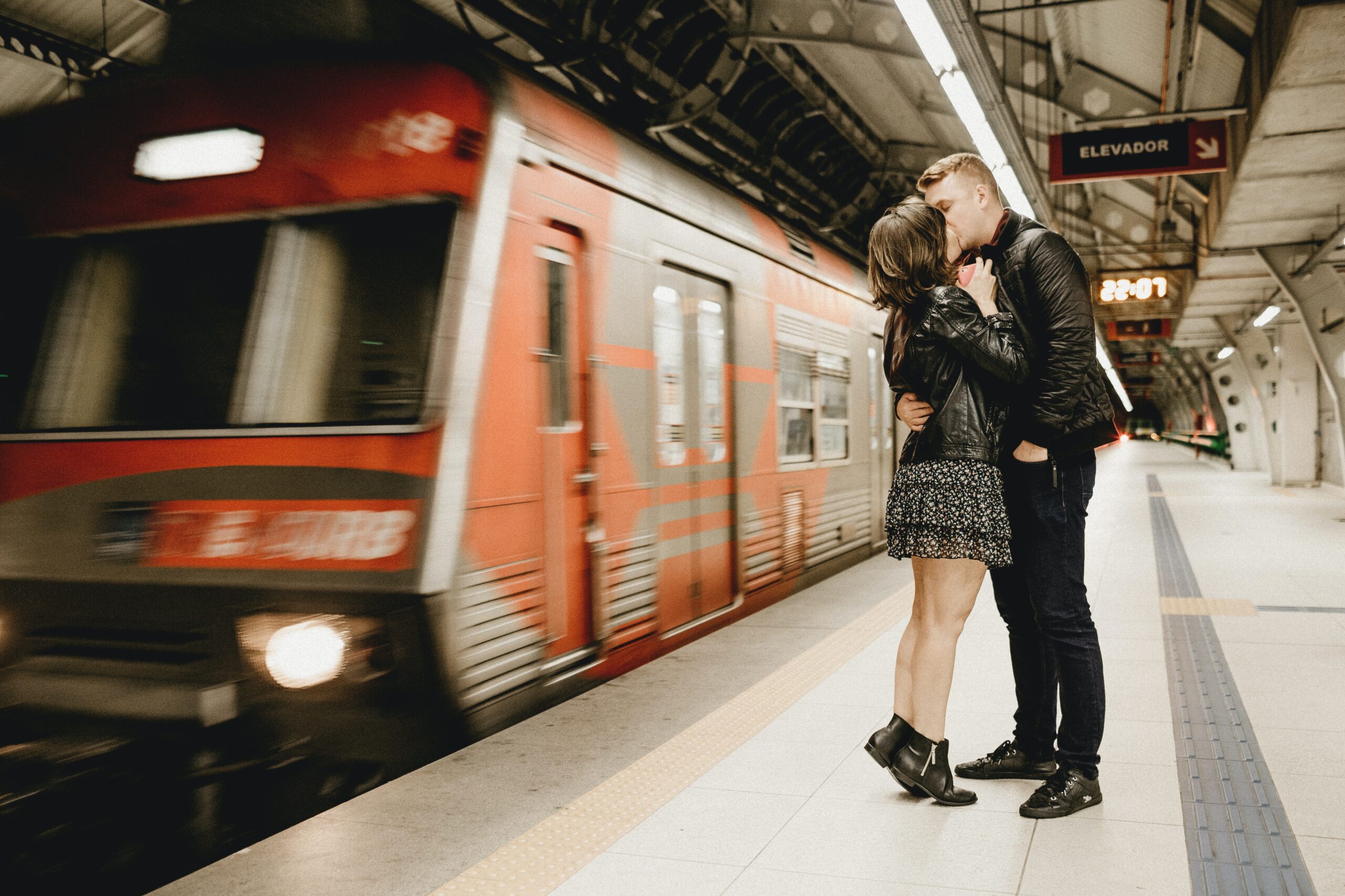 casal está se beijando enquanto um trem passa por trás em movimento.
