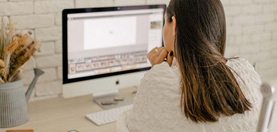Isis Castro está sentada em frente ao computador, pensativa com a mão no queixo escolhendo um curso de fotografia online