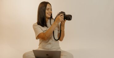 Isis está com seu notebook no colo e sua câmera fotografando na mão. Esta é uma foto para o lançamento do curso de fotografia online MOVE.